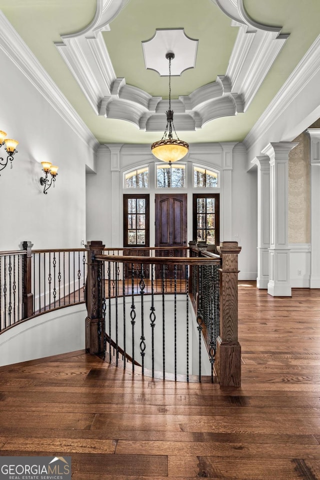 interior space featuring ornamental molding, a tray ceiling, ornate columns, and wood finished floors