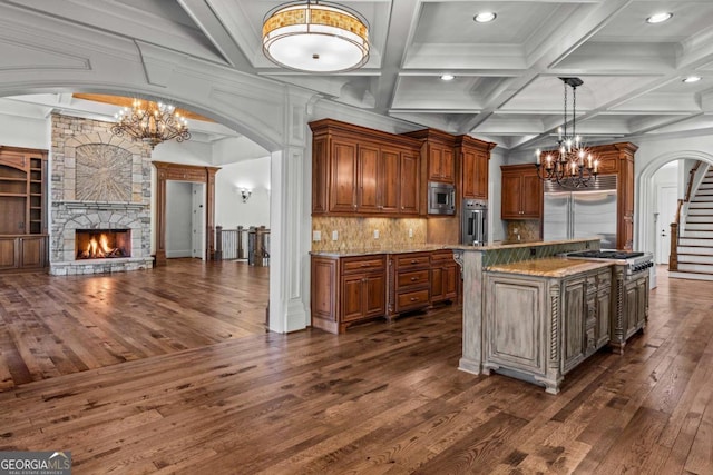 kitchen featuring an inviting chandelier, arched walkways, a stone fireplace, and built in appliances