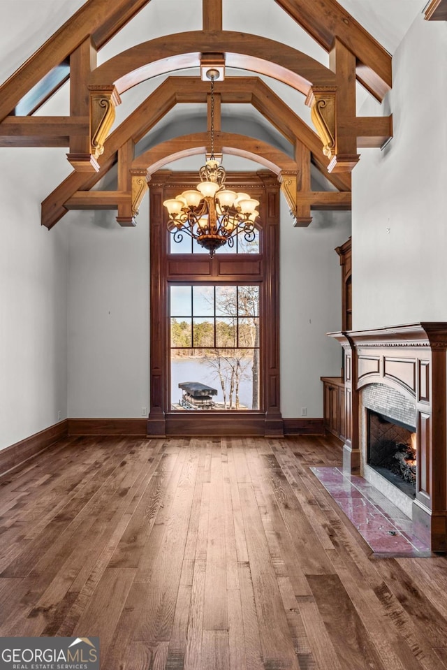 unfurnished living room featuring wood-type flooring, an inviting chandelier, a high end fireplace, high vaulted ceiling, and baseboards