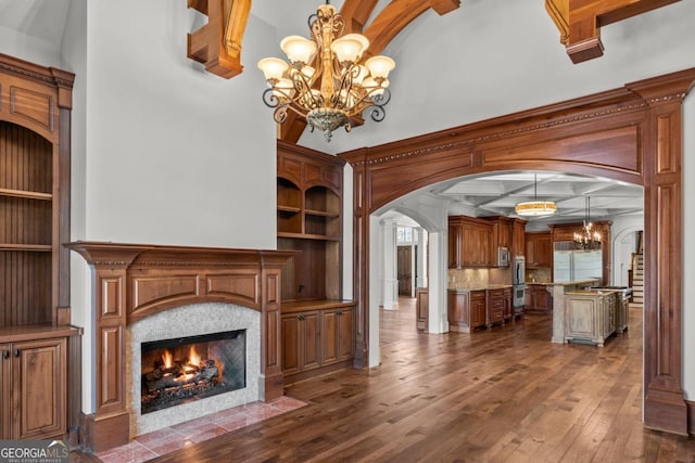 unfurnished living room featuring arched walkways, dark wood finished floors, a fireplace with flush hearth, a chandelier, and coffered ceiling