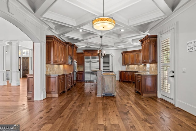 kitchen with arched walkways, stainless steel appliances, a center island, dark wood-style floors, and decorative columns