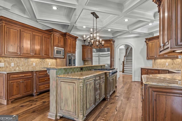 kitchen featuring light stone counters, arched walkways, a center island, dark wood-style floors, and built in appliances