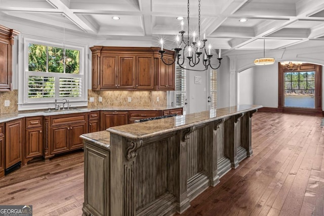 kitchen with arched walkways, hardwood / wood-style flooring, a center island, a chandelier, and a sink