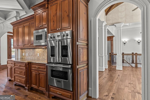 kitchen featuring decorative columns, appliances with stainless steel finishes, arched walkways, and dark wood-type flooring