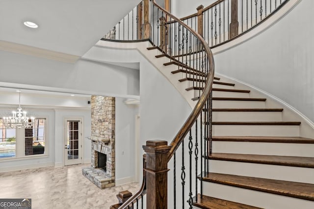 stairs featuring a chandelier, a fireplace, crown molding, and a towering ceiling