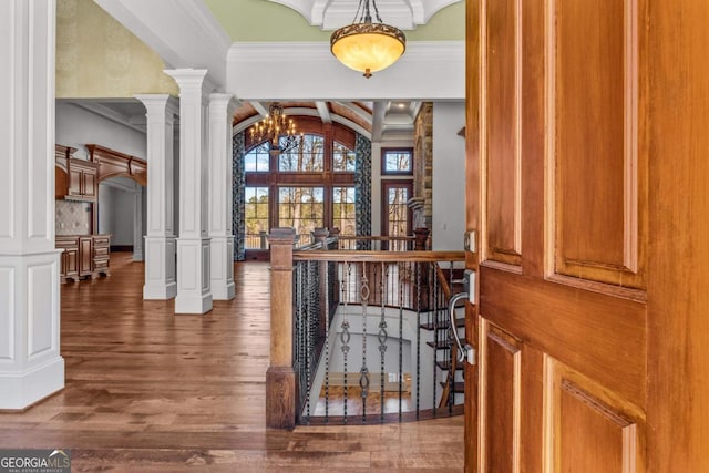 bar featuring arched walkways, decorative columns, ornamental molding, wood finished floors, and beamed ceiling