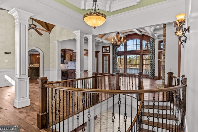 interior space featuring beam ceiling, a wainscoted wall, a high ceiling, wood finished floors, and ornate columns