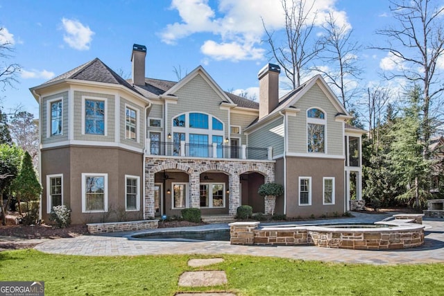 rear view of property featuring stone siding, a chimney, a balcony, and stucco siding