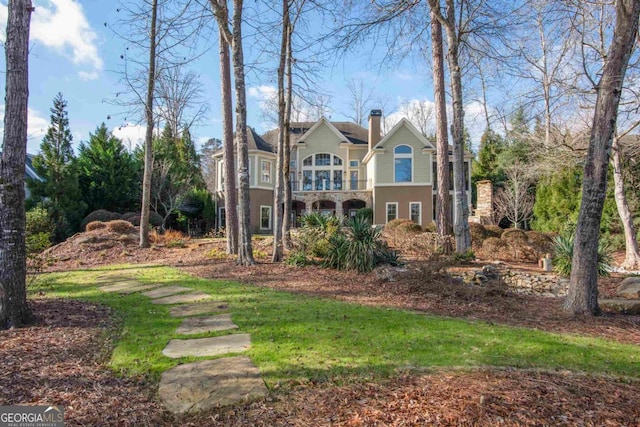 view of front of property with a balcony, stone siding, and a chimney