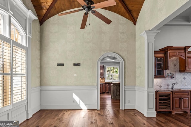 unfurnished dining area featuring wine cooler, arched walkways, dark wood-type flooring, high vaulted ceiling, and ornate columns