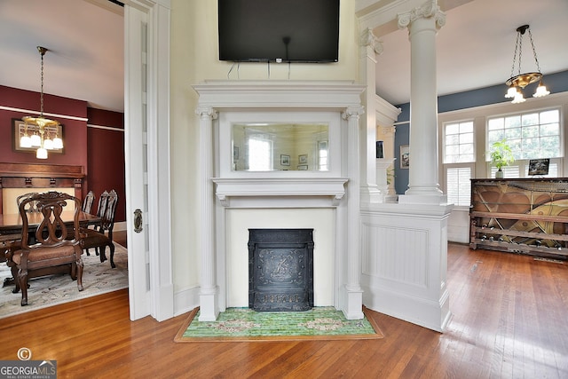 living room with a notable chandelier, ornate columns, a fireplace with flush hearth, and hardwood / wood-style flooring