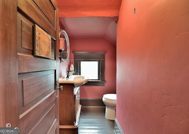 half bathroom with baseboards, toilet, wood finished floors, vaulted ceiling, and vanity