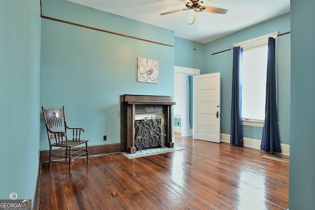 living area featuring a fireplace with flush hearth, baseboards, hardwood / wood-style floors, and a ceiling fan