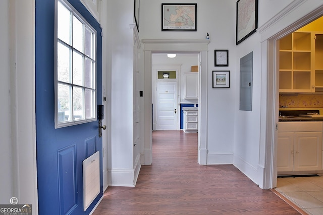 corridor featuring electric panel, baseboards, and wood finished floors