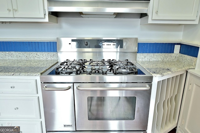 kitchen with white cabinets, wall chimney exhaust hood, light stone counters, and range with two ovens