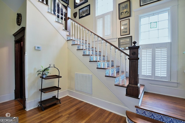 staircase featuring baseboards, a high ceiling, visible vents, and wood finished floors