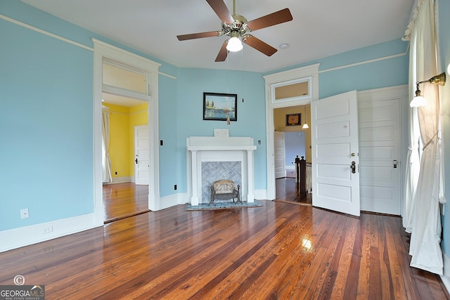 unfurnished living room featuring hardwood / wood-style floors, a premium fireplace, a ceiling fan, and baseboards