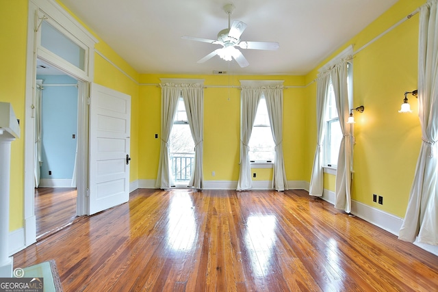 empty room featuring hardwood / wood-style flooring, visible vents, baseboards, and a ceiling fan