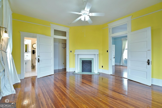 unfurnished living room featuring wood-type flooring, baseboards, a ceiling fan, and a fireplace with flush hearth