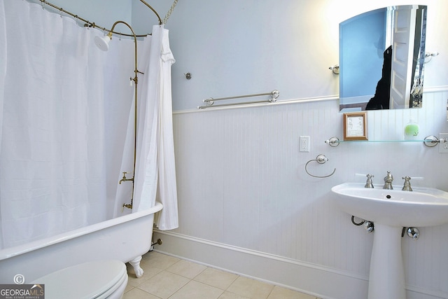 bathroom with toilet, a wainscoted wall, a sink, tile patterned floors, and shower / bath combination with curtain