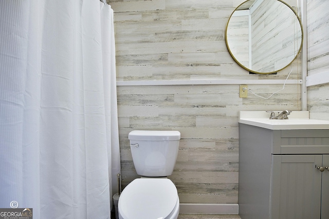 bathroom featuring vanity, toilet, and wooden walls