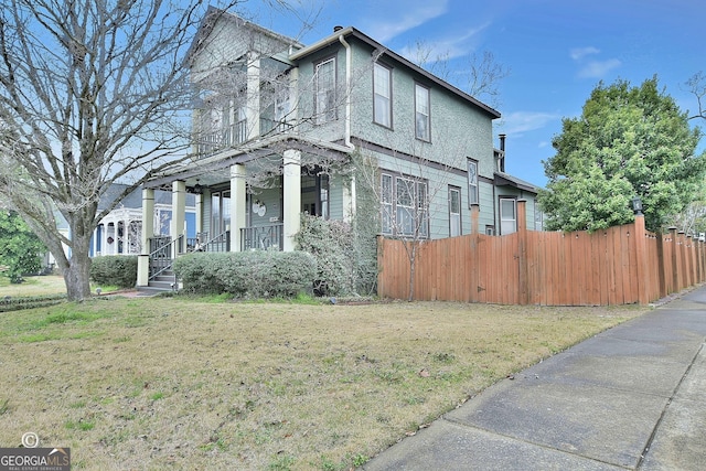 view of property exterior featuring covered porch, fence, and a lawn