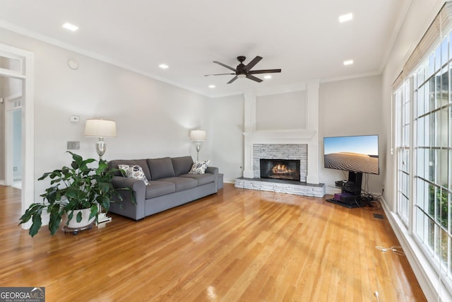 unfurnished living room featuring baseboards, a ceiling fan, ornamental molding, wood finished floors, and a stone fireplace