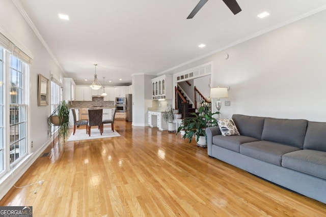 living room with ceiling fan, light wood-style flooring, recessed lighting, ornamental molding, and stairway