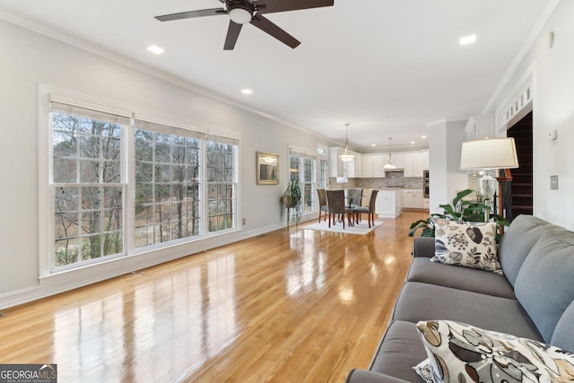 living area featuring recessed lighting, a ceiling fan, baseboards, light wood-type flooring, and crown molding