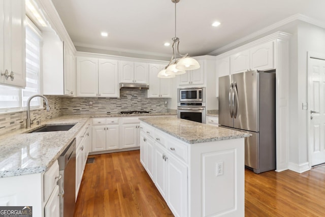 kitchen featuring under cabinet range hood, stainless steel appliances, a sink, backsplash, and a center island