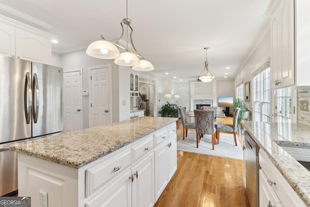 kitchen with pendant lighting, light wood-style flooring, a lit fireplace, appliances with stainless steel finishes, and crown molding