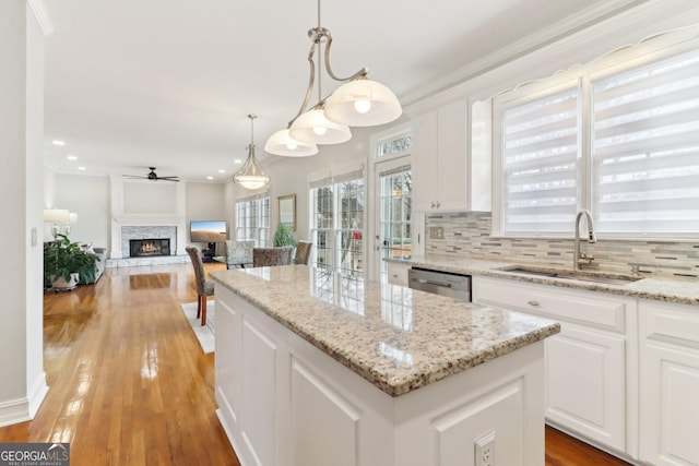 kitchen with light wood finished floors, backsplash, a kitchen island, a sink, and a stone fireplace