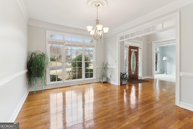 interior space with ornamental molding, plenty of natural light, wood finished floors, and an inviting chandelier