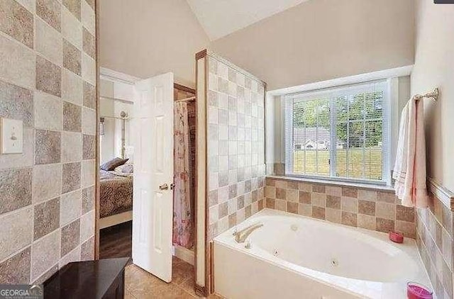 ensuite bathroom with a garden tub, tile walls, ensuite bathroom, vaulted ceiling, and tile patterned flooring