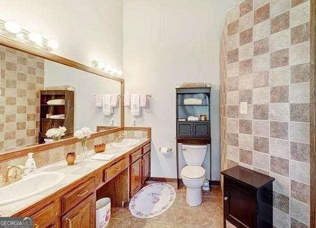 bathroom with double vanity, a sink, toilet, and tile patterned floors