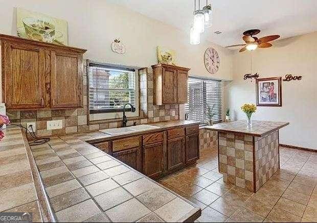 kitchen with tile counters, a center island, a sink, a high ceiling, and backsplash