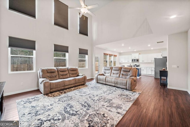 living room featuring recessed lighting, dark wood-type flooring, a towering ceiling, a ceiling fan, and baseboards