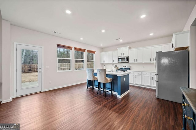 kitchen with visible vents, an island with sink, dark wood-style floors, appliances with stainless steel finishes, and white cabinetry