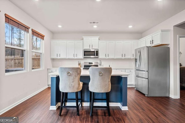 kitchen with white cabinets, appliances with stainless steel finishes, dark wood-style flooring, a kitchen island with sink, and light countertops