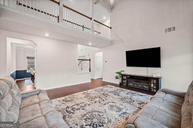 living room with visible vents, a high ceiling, a glass covered fireplace, wood finished floors, and baseboards