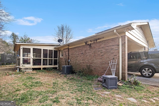 view of side of property with brick siding, central AC, a trampoline, and a sunroom