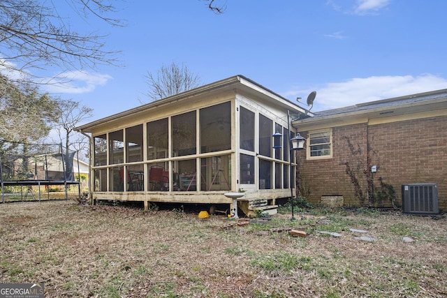 back of house with a trampoline, central AC unit, brick siding, and a sunroom