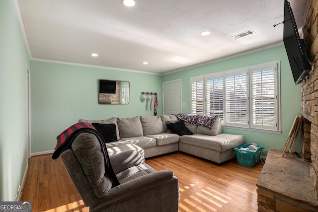 living room featuring wood finished floors, baseboards, visible vents, a fireplace, and ornamental molding