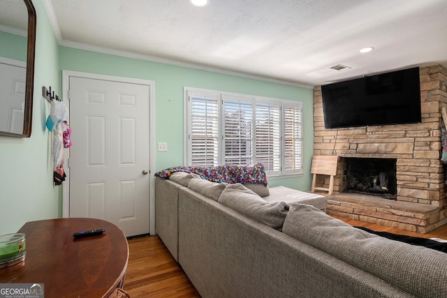 living room featuring light wood-type flooring, visible vents, recessed lighting, a fireplace, and crown molding