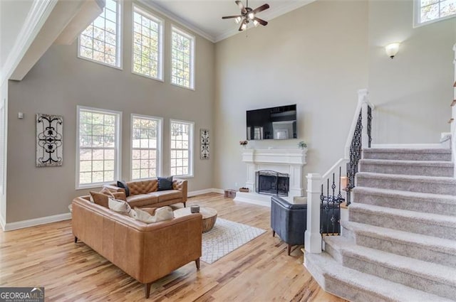 living area with stairway, a healthy amount of sunlight, a fireplace with raised hearth, ornamental molding, and light wood-type flooring