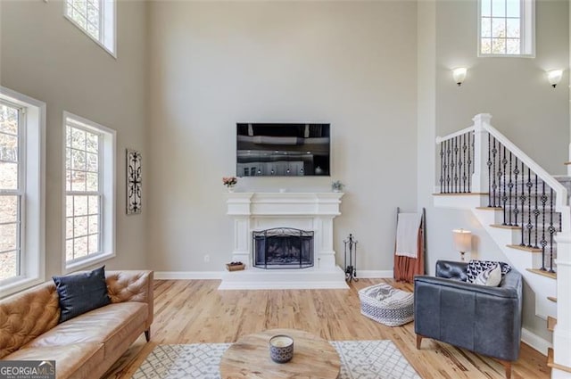 living room with wood finished floors, stairway, a fireplace with raised hearth, and a healthy amount of sunlight