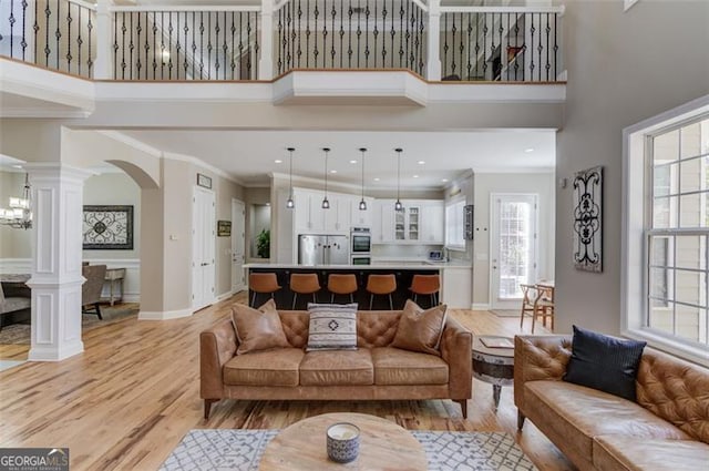 living area featuring light wood-type flooring, a high ceiling, crown molding, and ornate columns