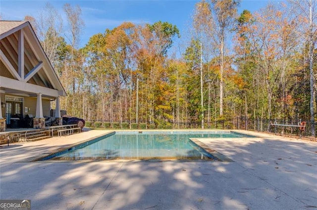 view of swimming pool with a forest view, a fenced in pool, a patio, and fence