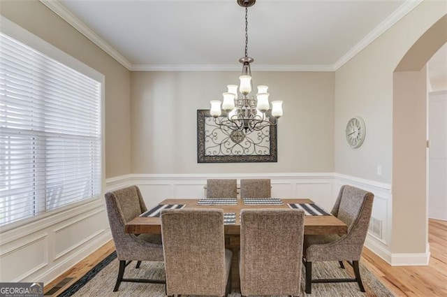 dining area featuring crown molding, light wood-style flooring, a notable chandelier, and arched walkways