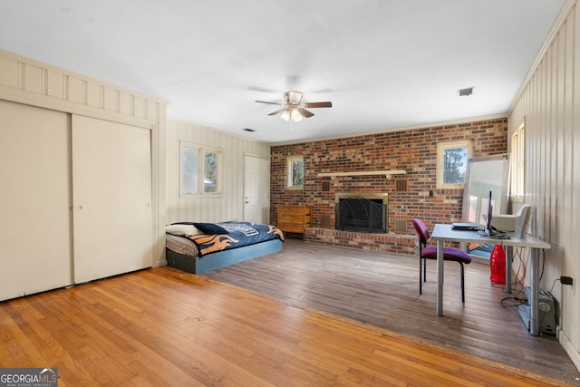 living room with brick wall, a fireplace, visible vents, a ceiling fan, and hardwood / wood-style floors